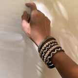 Nayla Handwoven Rattan Bracelet on a wrist, featuring unique handcrafted patterns in natural and black colors. Made by women artisans in Borneo Island, Indonesia, with a 6cm diameter. Each bracelet is one-of-a-kind, reflecting the artisan's creativity.