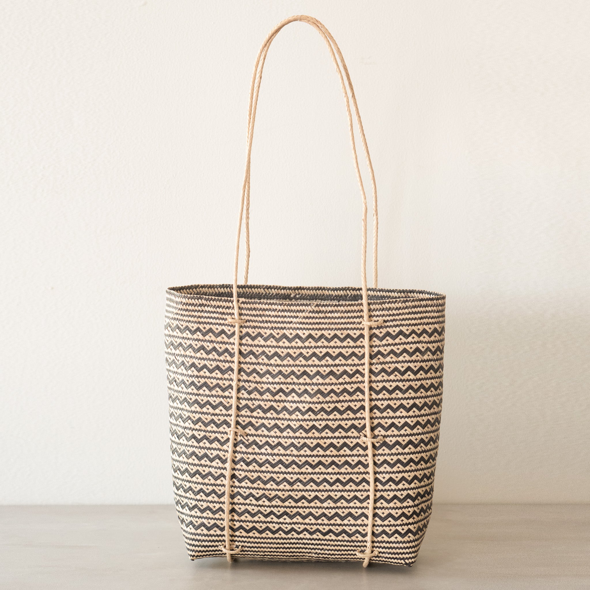 Anya Handwoven Rattan Shoulder Bag, a lightweight and durable summer bag crafted from natural rattan, featuring a stylish zigzag pattern and long handles, handwoven by women artisans in Borneo, Indonesia. Ideal for beach trips or as a work bag, capable of holding up to 3kg