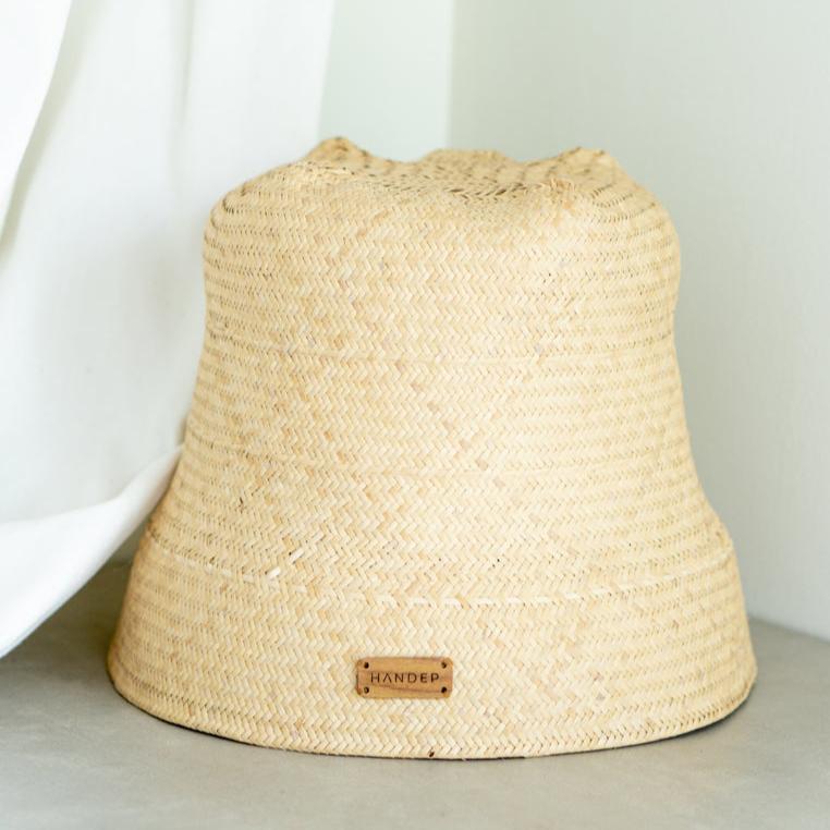 Hannah Foldable Rattan Handwoven Bucket Hat in a natural beige color. This eco-friendly, lightweight hat features a soft, handwoven rattan texture that is both durable and flexible, making it easy to fold and pack. The classic bucket hat design offers comfortable sun protection, perfect for casual outings and summer adventures